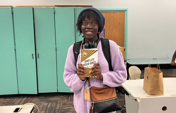 student smiling holding an amplify your voice booklet